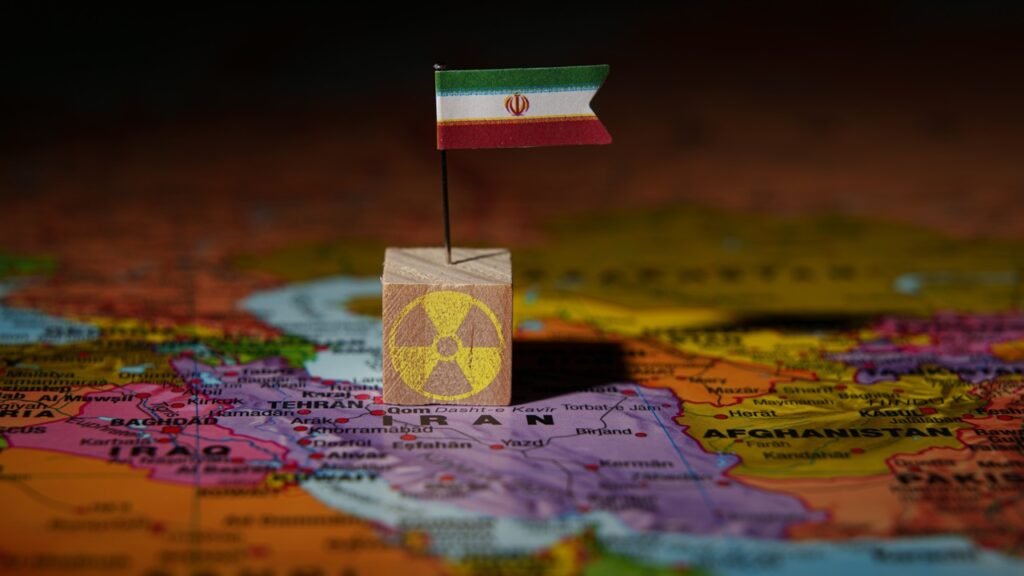 Can Iran’s Nuclear Program Really Be Stopped? A small Iranian flag pinned into a wooden block featuring a yellow radioactive symbol, placed directly over the map of Iran to illustrate the geopolitical impact of Iran Nuclear Ambitions and its regional influence.