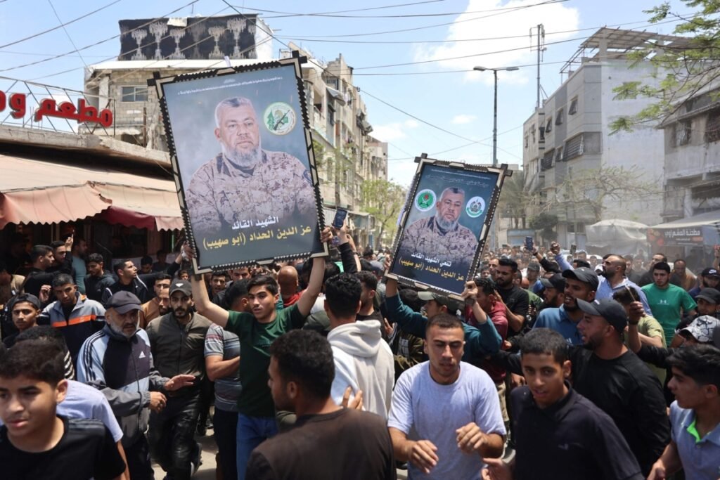 A large crowd of demonstrators marches down a city street, hoisting two large framed posters of a deceased military commander, underscoring the deep-seated public mobilization that complicates regional political initiatives and Hamas disarmament.