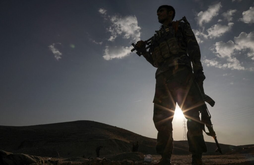 Silhouette of an armed Kurdish Peshmerga fighter standing on a hill with a rifle as the sun breaks through in the background, providing context to the strategic decisions of Iran's militant Kurds.
