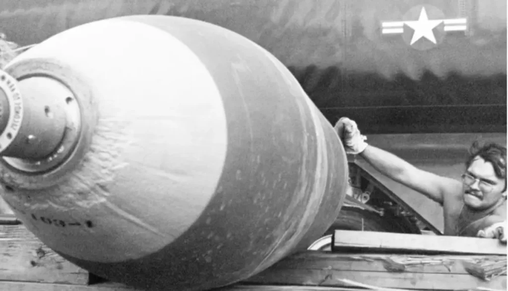 A black and white historical photograph showing a massive aerial bomb being handled by a crew member next to an aircraft featuring a U.S. military star insignia, providing a powerful visual context for the evolution of aerial warfare and the "secrets" of military history often associated with an Iran War bombing.