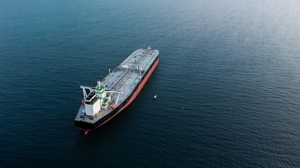 An aerial drone shot of a massive industrial oil tanker navigating through open blue waters, illustrating the global shipping dynamics and energy bottlenecks linked to Iran's Leverage in maritime conflicts.