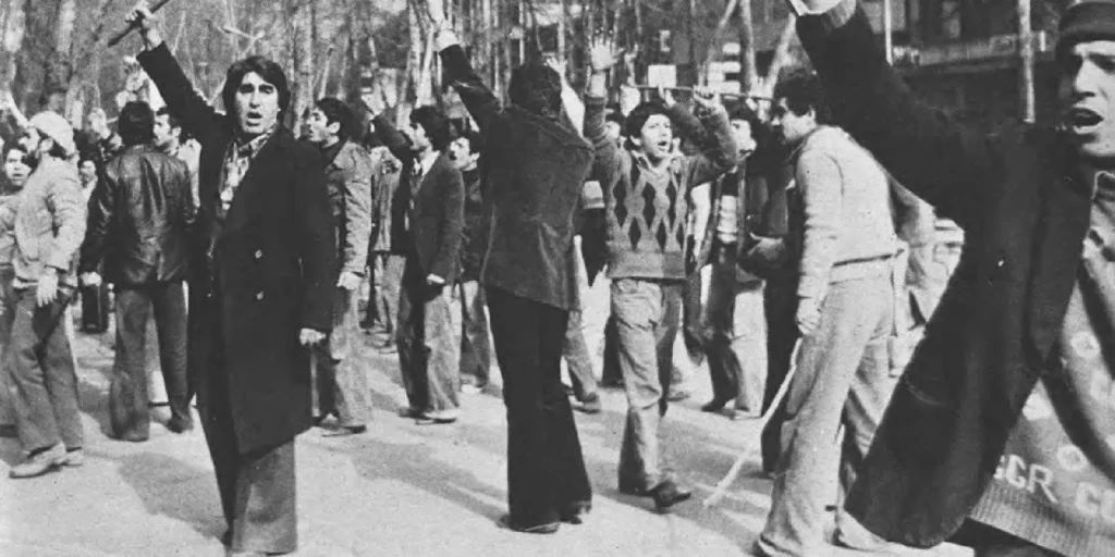 A vintage black-and-white photograph of Iranian protesters raising their fists during a historic street demonstration, reflecting the long-standing public sentiment and domestic roots that continue to influence regional tensions and the potential for a US Israel Iran War.