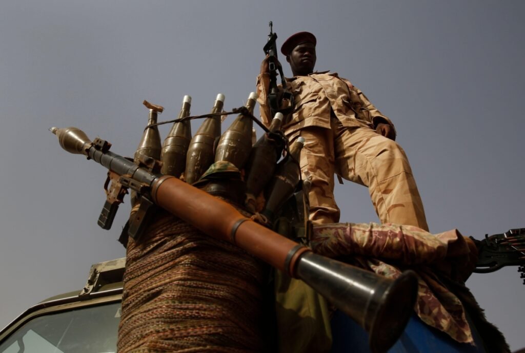 Vanishing horizon: why Sudan’s civil war is getting harder to solve A low-angle shot of a soldier in desert camouflage uniform standing on a military vehicle next to a mounted rocket-propelled grenade (RPG) launcher and an array of warheads, illustrating the heavy militarization defining Sudan's civil war.