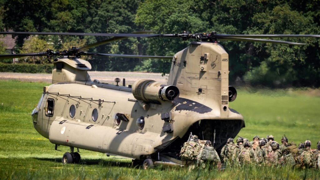 Military personnel carrying tactical gear board a large, double-rotor Boeing CH-47F Chinook helicopter through its open rear ramp on a grassy field, showcasing the logistics and troop movements that project American power.