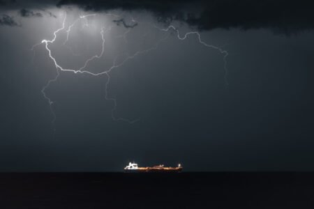 A dramatic night view of an oil products tanker illuminated on dark open waters under a sky filled with lightning strikes, providing visual context for the market disruptions analyzed in the MENA Energy Recap.