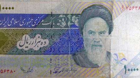 A close-up of a ten-thousand Iranian Rial banknote featuring the portrait of Ayatollah Ruhollah Khomeini, illustrating the historical symbols and institutional establishment of clerical rule.