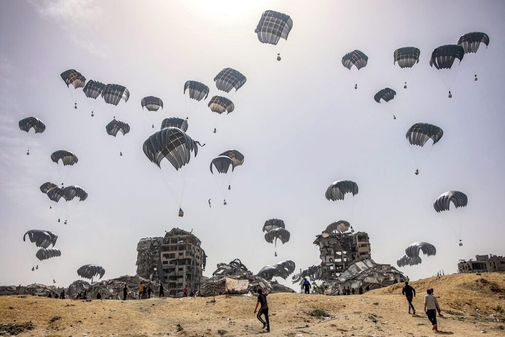 How Aid to Gaza Compares Across Arab Countries Numerous cargo parachutes deploy in the air to deliver supplies over a wide landscape of heavily damaged buildings, capturing the aerial drop logistics used for Aid to Gaza.