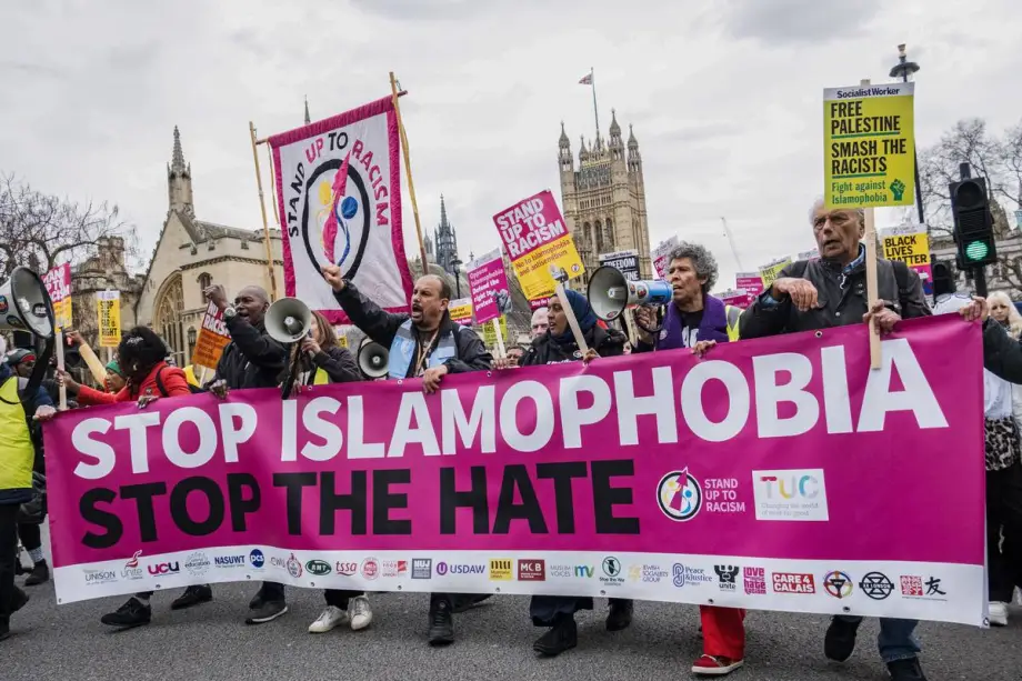 The rise of Reform UK and Islamophobia Demonstrators march through central London holding a prominent pink banner reading "STOP ISLAMOPHOBIA STOP THE HATE" with the Palace of Westminster in the background, highlighting the societal tensions surrounding Islamophobia in uk.