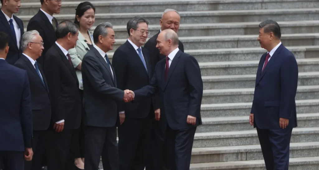 هل عاد بوتين من الصين خالي الوفاض؟ Russian President Vladimir Putin shaking hands with Chinese Foreign Minister Wang Yi while Xi Jinping stands alongside officials on outdoor stone steps, capturing the diplomatic meetings leading to the analysis of a Putin Return From China.
