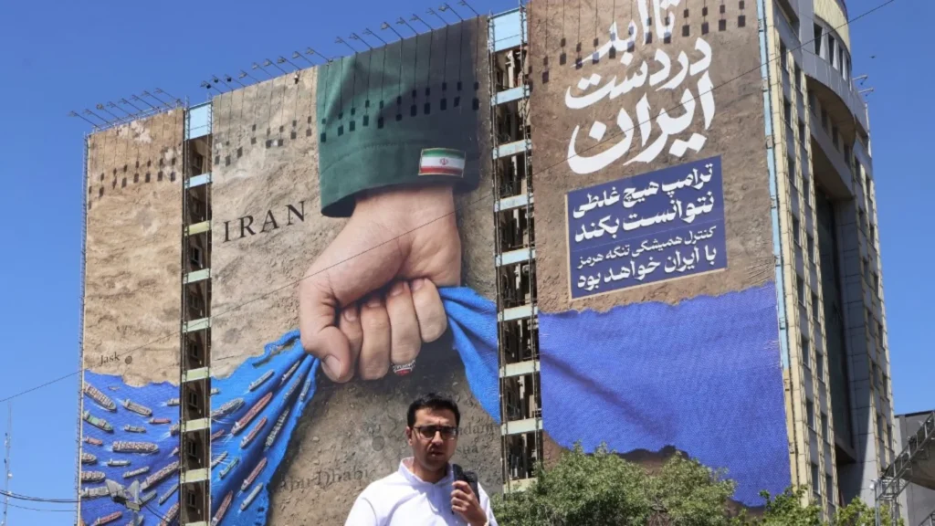 A massive geopolitical billboard at Tehran’s Vanak Square depicting a giant fist clenched over shipping lanes in the Strait of Hormuz, visually illustrating the perspective that Iran has won the war.