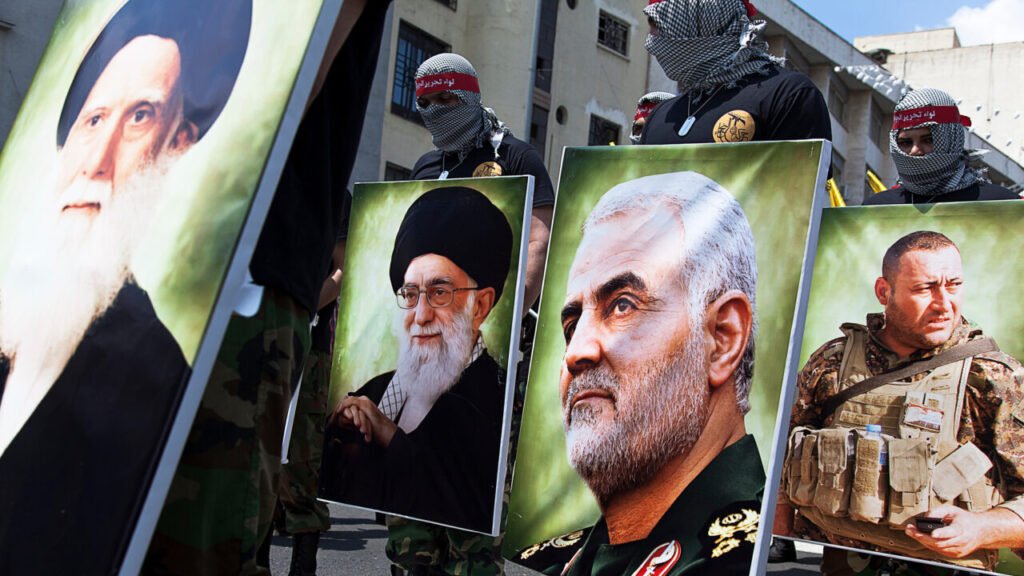Can Iran’s ‘Axis of Resistance’ Rebound? Fighters with covered faces and red headbands holding large portraits of Qasem Soleimani and Ali Khamenei during a parade, illustrating the political and ideological unity of Iran's Axis of Resistance.