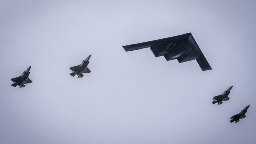 A formation of advanced military aircraft including a B-2 Spirit stealth bomber and F-35 fighter jets flying in formation, symbolizing the massive military escalation and Iran war existential stakes that make peace negotiations critically urgent.