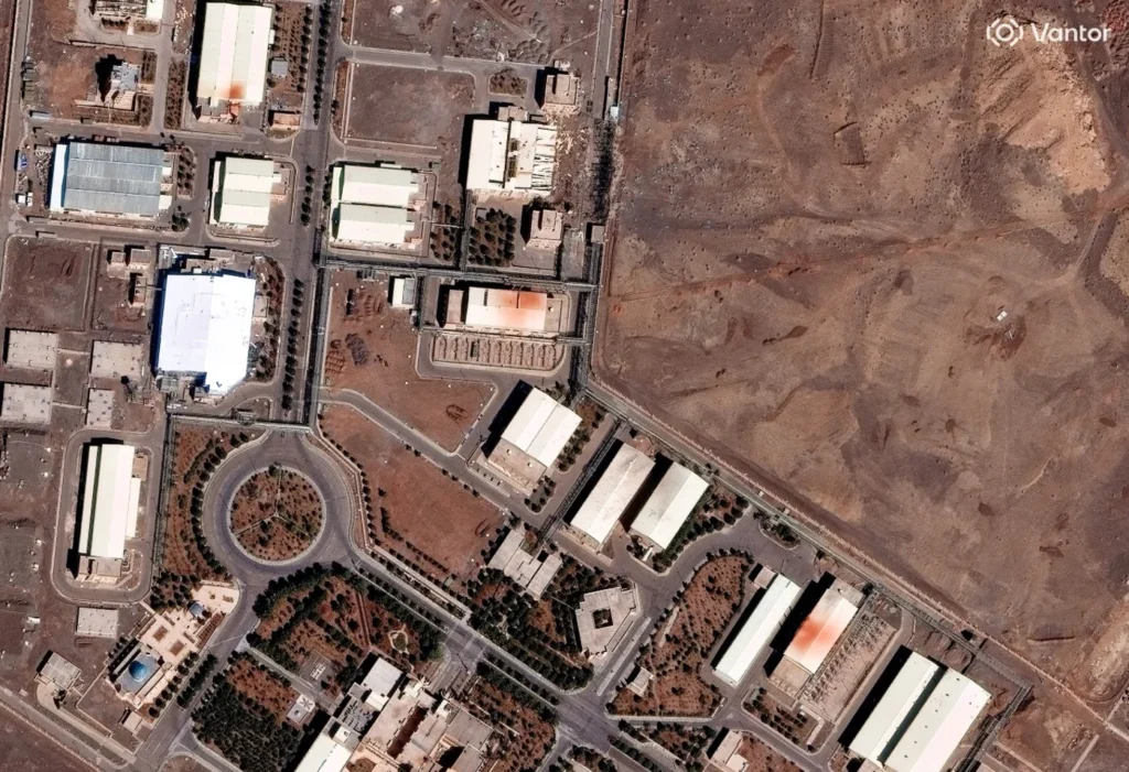 A high-resolution satellite view of a nuclear facility with industrial warehouses and circular roadways, illustrating the transparency challenges and monitoring complexities that define the current NPT credibility crisis and the strategic lessons learned from the Iranian nuclear program.