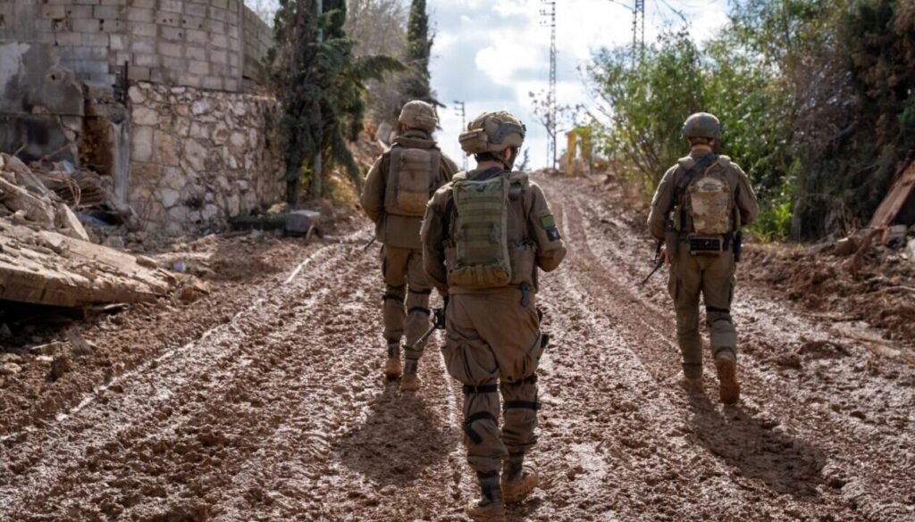 Why You Shouldn’t Dismiss the Lebanon-Israel Peace Talks Three IDF soldiers wearing full combat gear and backpacks patrol away from the camera down a heavily rutted, muddy dirt road in Southern Lebanon, providing a stark ground-level perspective on the regional instability driving the Lebanon-Israel Peace Talks.