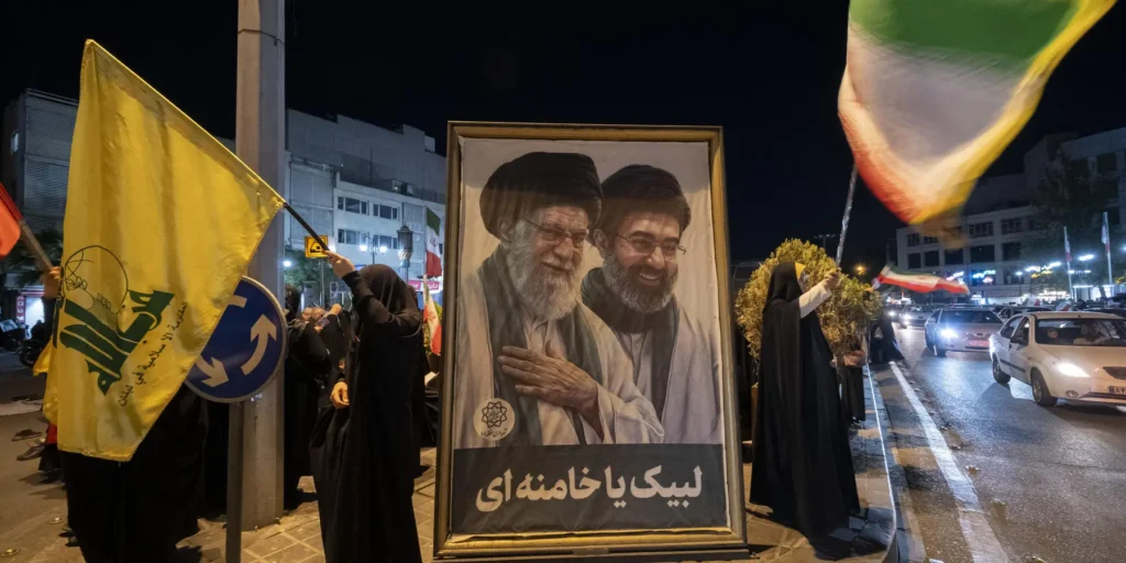 A public demonstration at night featuring a framed portrait of Iranian leadership next to individuals waving flags, providing the geopolitical context for the strategic threat to hit the UAE if escalation reaches Lebanon.
