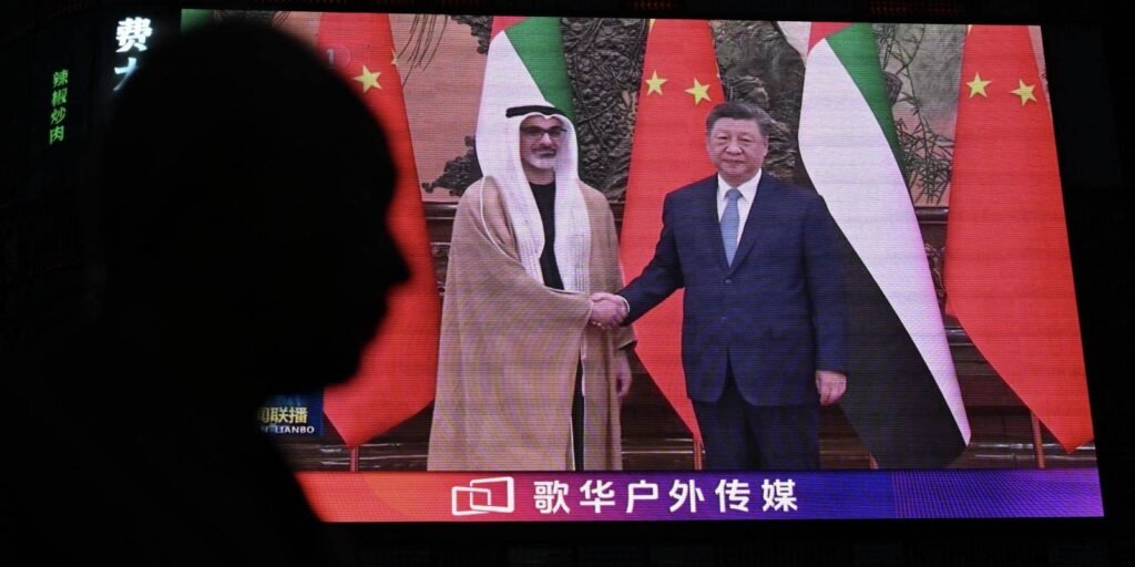 A silhouette of a person looking at a bright digital screen displaying UAE President Sheikh Mohamed bin Zayed Al Nahyan shaking hands with Chinese President Xi Jinping, symbolizing the growing public awareness and geopolitical visibility of the China Gulf Strategy in the evolving post-war regional order.