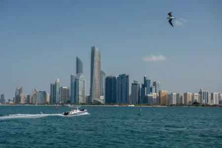 The modern skyline of Abu Dhabi along the turquoise waters of the Persian Gulf, with a speedboat cruising in the foreground and a seagull flying above, capturing the economic power and strategic independence driving the UAE exit from OPEC.