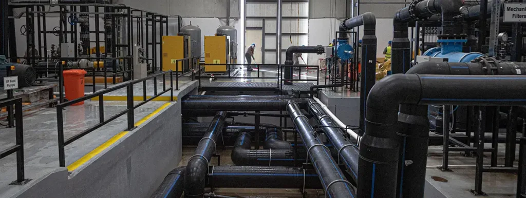 Water and Cognitive Warfare An industrial water treatment facility featuring a network of large blue and black pipeline systems, valves, and filtration equipment, illustrating the infrastructure vulnerabilities analyzed within Water and Cognitive Warfare.