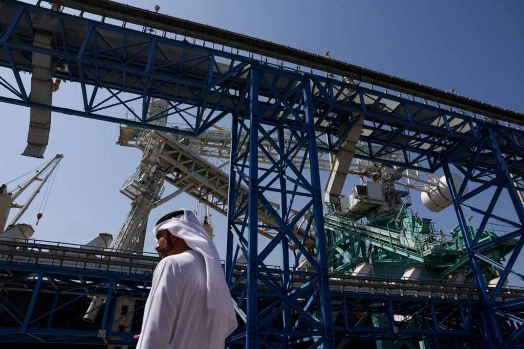 A man in traditional white Emirati dress walks past a massive blue industrial gantry at the Port of Fujairah, illustrating the strategic importance and economic risks of Gulf States Security during the regional maritime crisis.