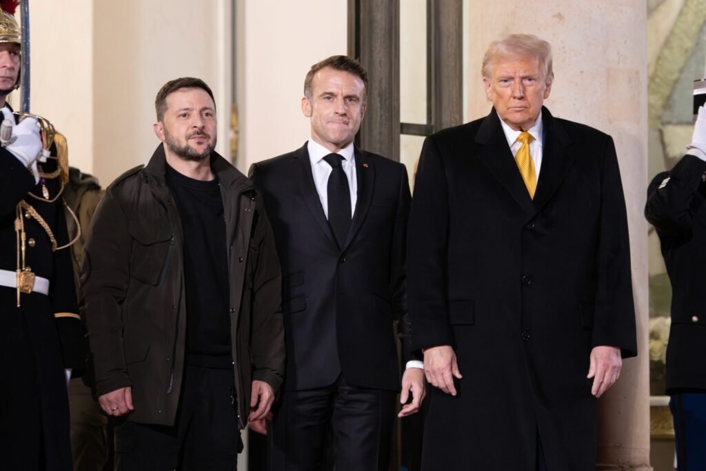 Ukrainian President Volodymyr Zelenskyy, French President Emmanuel Macron, and Donald Trump standing together during a high-level summit to discuss geopolitical strategy and the potential impacts of a Transatlantic Iranian Blockade on global security.