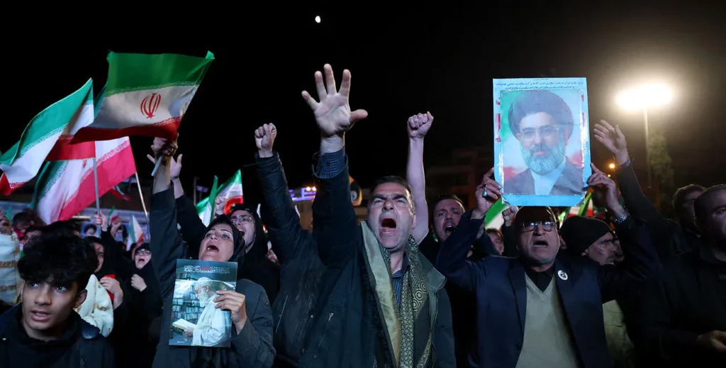 Crowds holding Iranian flags and portraits during a nighttime demonstration, capturing the public atmosphere and regional reactions surrounding the 2026 Iran Ceasefire.