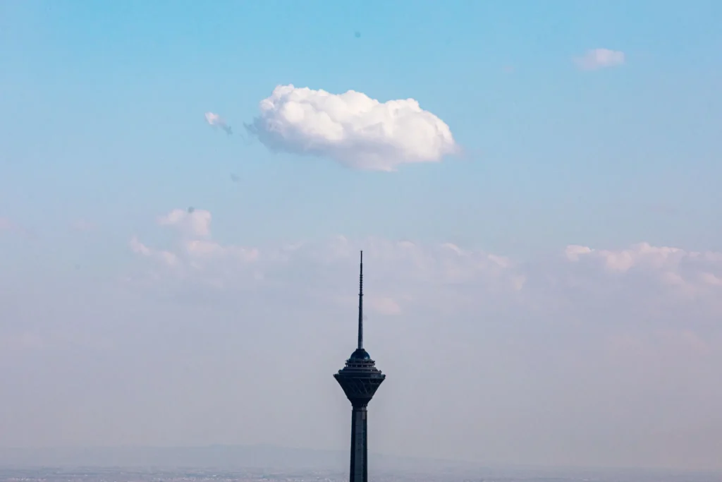 The Milad Tower in Tehran standing under a clear sky with a single white cloud, representing the calm before a potential Trump Iran War and the geopolitical tension surrounding the region.