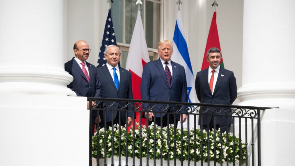 US President Donald Trump, Israeli Prime Minister Benjamin Netanyahu, and dignitaries from Bahrain and the UAE stand together on the White House balcony with national flags behind them, illustrating the diplomatic framework underlying The Abraham Accords' Evolution.