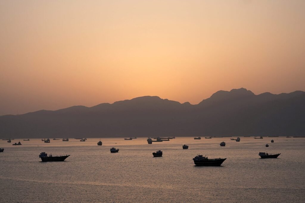 Traditional dhows and cargo vessels anchored in the calm waters of the Strait of Hormuz at sunset, illustrating the critical maritime chokepoint and the strategic vulnerabilities that define the current regional crisis.