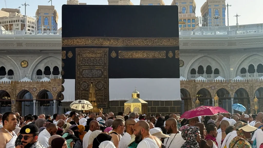 A dense crowd of Muslim pilgrims gathered in the courtyard of the Grand Mosque in Mecca, walking past the Kaaba under umbrellas, highlighting the profound spiritual longing disrupted globally by Israel's war on Gaza.
