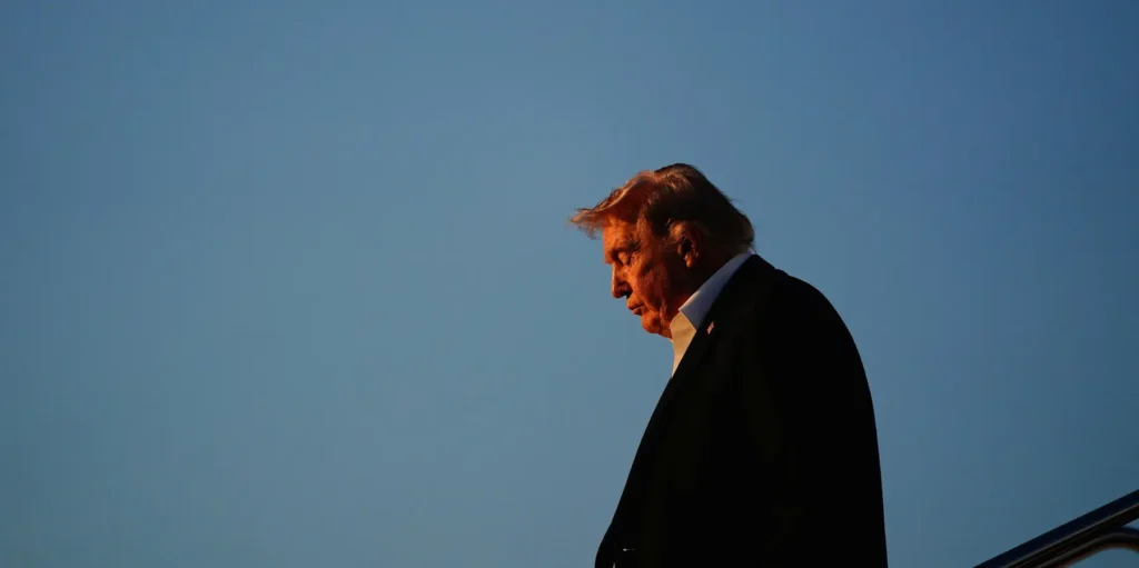 Profile of Donald Trump in a pensive stance against a vast blue sky at sunset, symbolizing the internal and external pressures leading to the potential American primacy collapse.