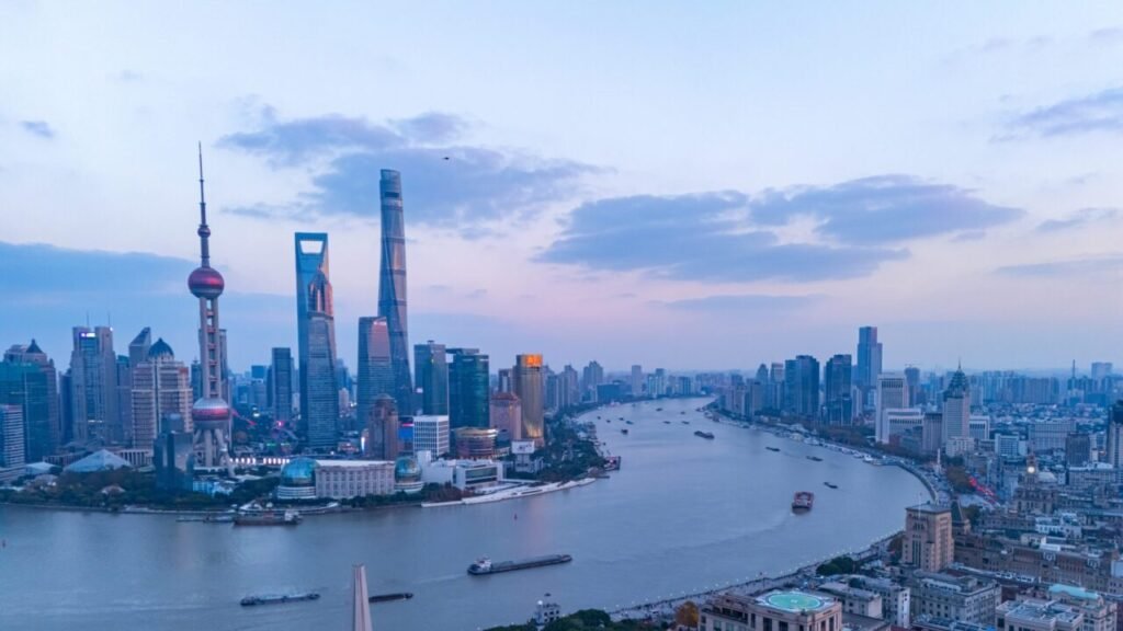 Why China’s Economy Is Weaker Than You Think An aerial panorama of the Shanghai skyline along the Huangpu River featuring the Oriental Pearl Tower and skyscrapers at dusk, providing visual context to the ongoing structural challenges within China's economy.