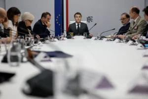 French President Emmanuel Macron sits at the head of an oval conference table during an official state meeting with military and civilian advisors, contextualizing the strategic discussions necessary to cooperate in the Middle East.