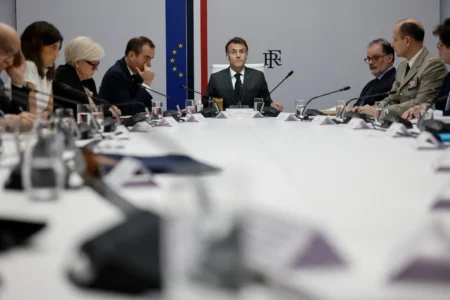 French President Emmanuel Macron sits at the head of an oval conference table during an official state meeting with military and civilian advisors, contextualizing the strategic discussions necessary to cooperate in the Middle East.