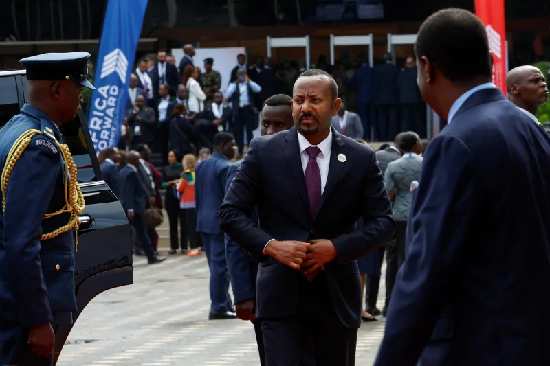 The War in Ethiopia Isn’t Over Ethiopian Prime Minister Abiy Ahmed, wearing a dark suit and purple tie, walks past military personnel and diplomats at an event in Nairobi, providing critical context on the regional diplomatic developments surrounding The War in Ethiopia.