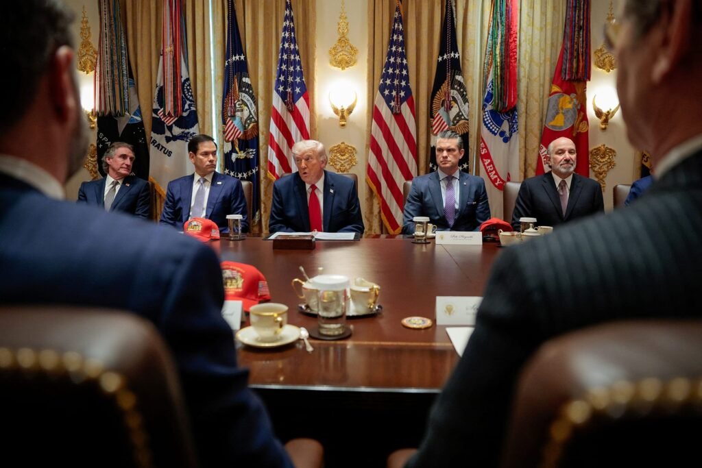 Donald Trump speaking at a conference table flanked by Marco Rubio and Pete Hegseth with American flags in the background, highlighting the political pressure surrounding U.S. foreign policy and the strategic Iran clock.