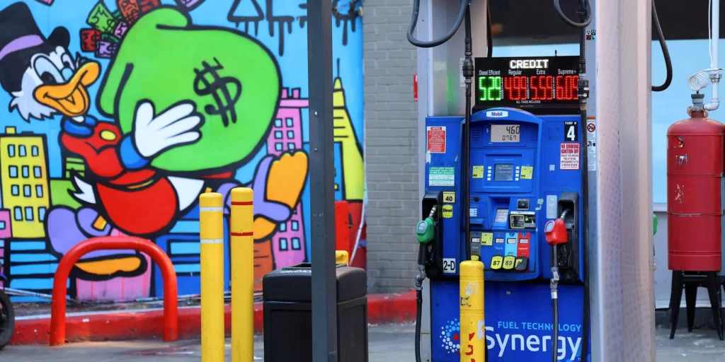 A US gas station pump with high fuel prices and money-themed graffiti, illustrating the disproportionate oil shock impact on the American economy.