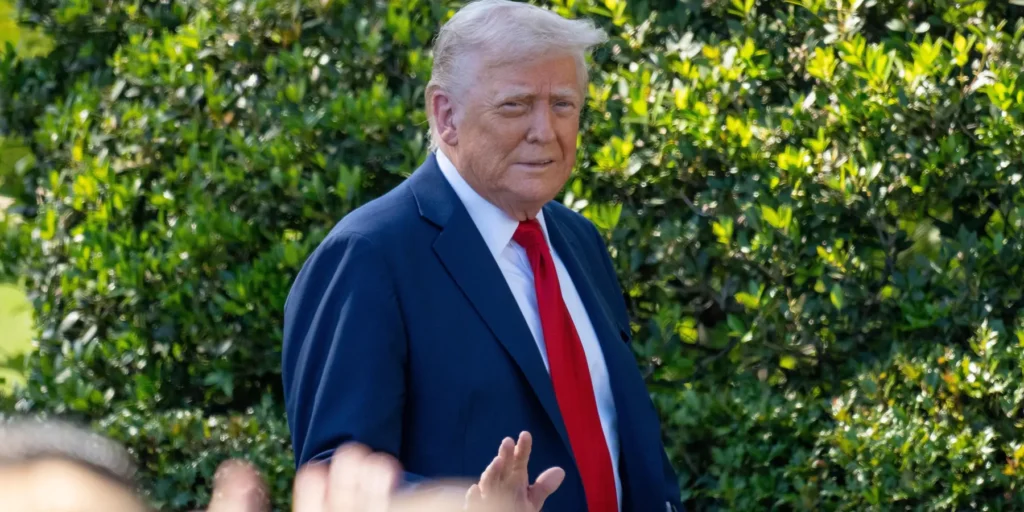 A medium shot of US President Donald Trump waving to a crowd in front of a green hedge backdrop, capturing the geopolitical shifts and political discourse surrounding a potential iran deal.