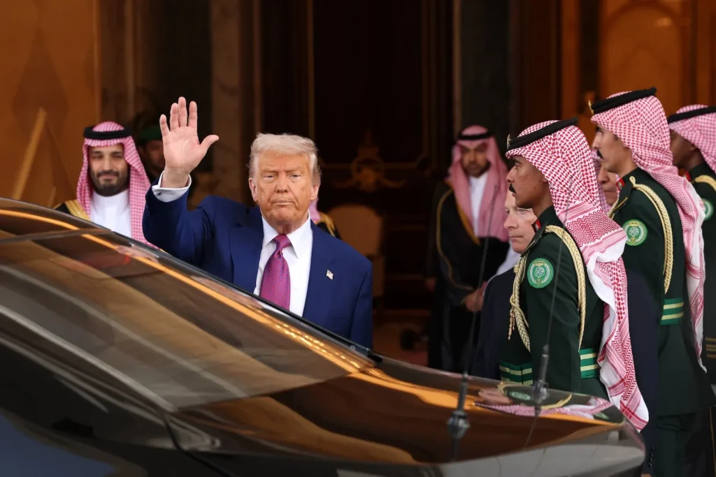 U.S. President Donald Trump waving his hand next to a black vehicle during an official visit in Saudi Arabia, surrounded by Crown Prince Mohammed bin Salman and Saudi royal guards, highlighting the strategic diplomatic engagements necessary because the US Can’t Win the Middle East.