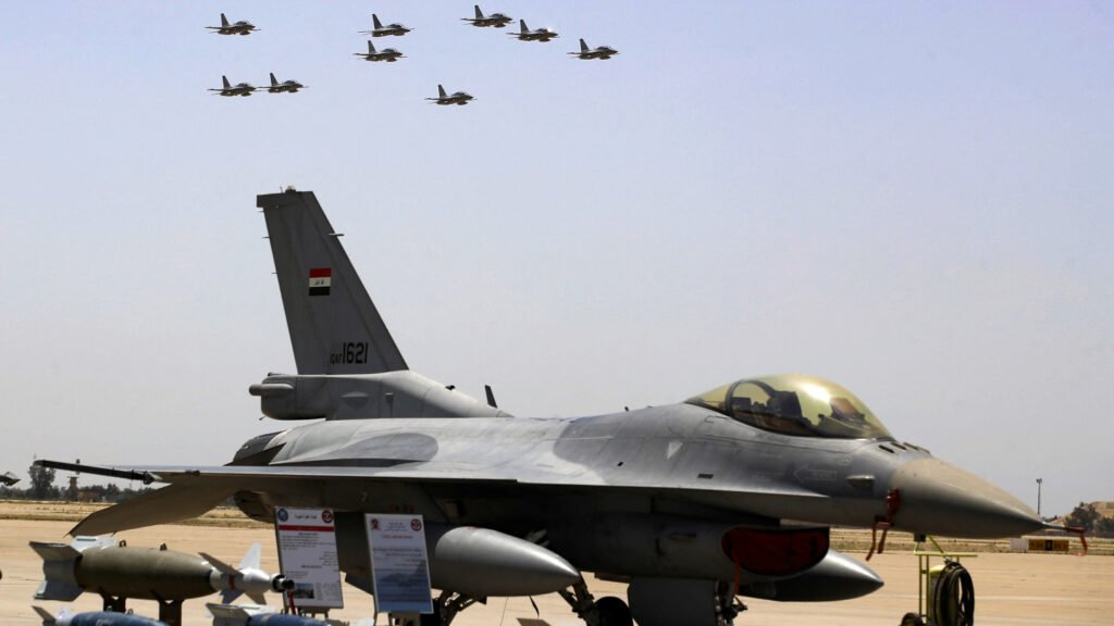An Iraqi Air Force F-16 fighter jet parked on an airfield tarmac with ordnance displayed nearby, while a formation of military aircraft flies in the sky above, capturing the strategic modernization efforts central to Iraq's race to rebuild.