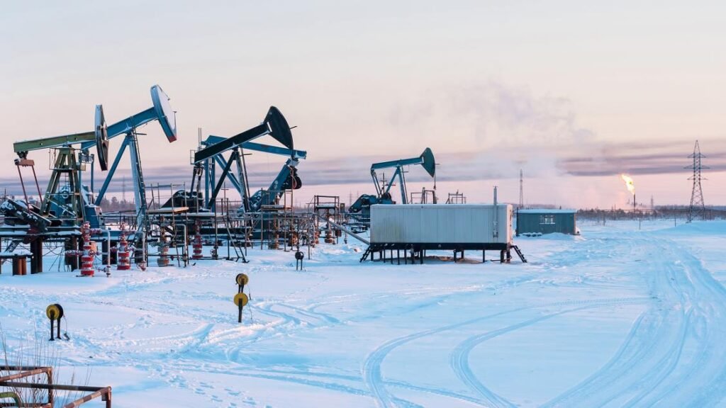 An industrial oil field in a snowy Siberian landscape with active pumpjacks and a gas flare burning in the distance, representing the infrastructure driving Russia's oil production.