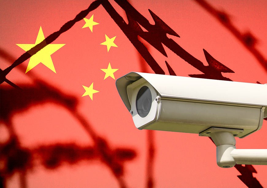 التجسس من خلال الانفتاح: تحليل الوضع الاستخباراتي الجديد للصين A white security surveillance CCTV camera is mounted in the foreground with silhouettes of sharp razor wire overlaying the national flag of China, conceptually representing state surveillance and China's intelligence posture.