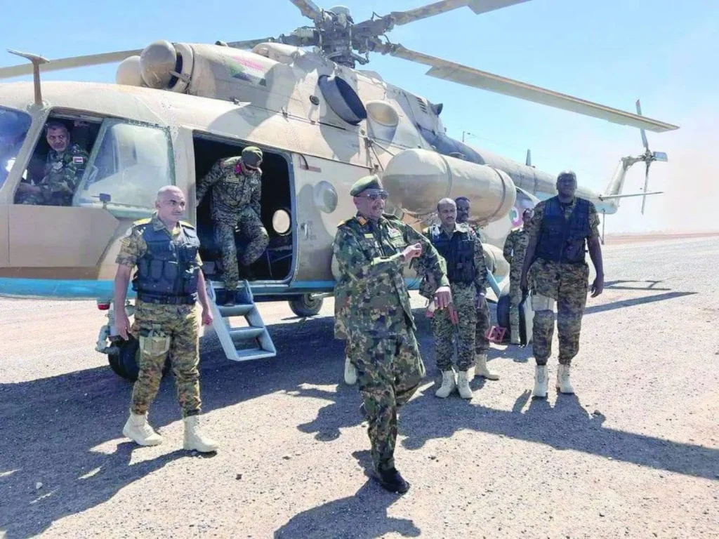 سودان از تسلیحات ایرانی فاصله میگیرد تا نظر واشنگتن را جلب کند Sudanese military commander Abdel Fattah al-Burhan steps away from a military transport helicopter surrounded by armed soldiers on a desert tarmac, providing context to Khartoum's shifting procurement strategies away from Iranian weapons.