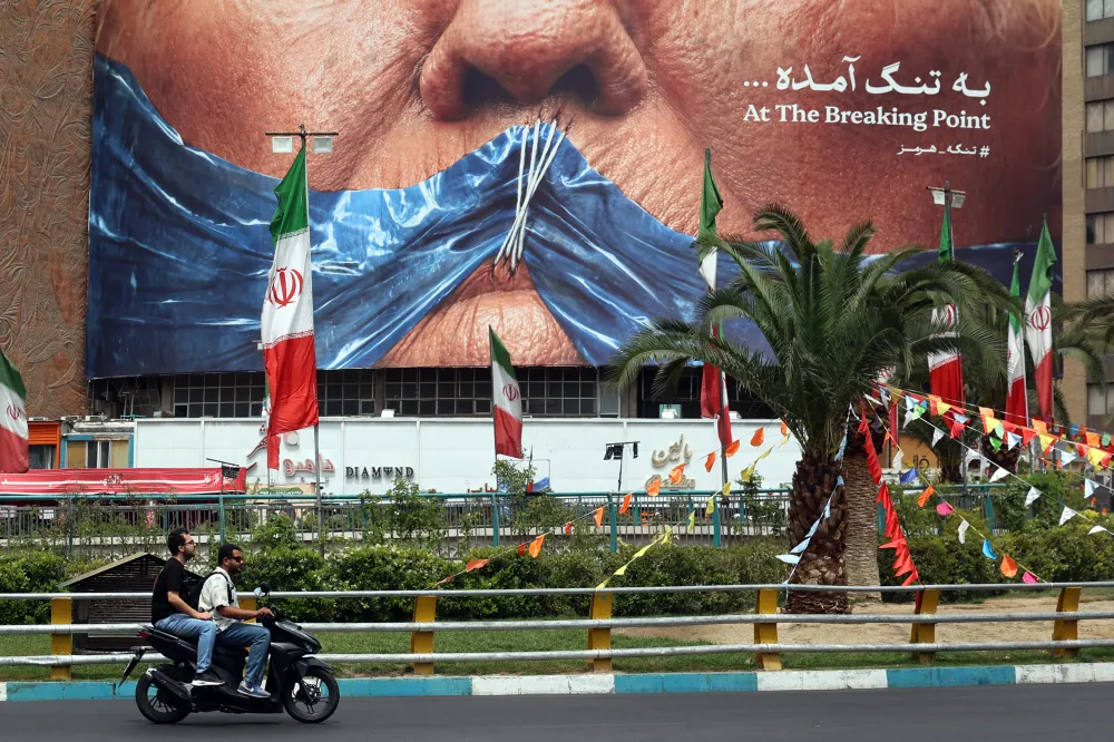 Necessity Is the Mother of Reinvention for Iran A street view in Tehran's Valiasr Square showing individuals riding a scooter past Iranian flags and a massive anti-Trump billboard reading "At The Breaking Point" with a hashtag for the Strait of Hormuz, capturing the geopolitical pressure driving a strategic Reinvention for Iran.