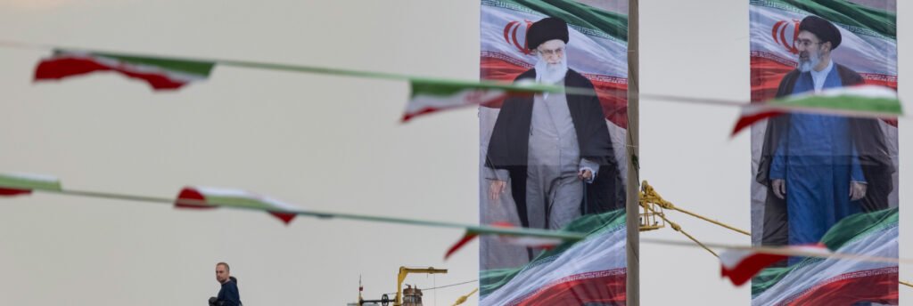 Pathways for the War with Iran An Iranian man walking in the lower left corner against a backdrop of large outdoor vertical banners displaying portraits of late Supreme Leader Ayatollah Ali Khamenei and his successor, draped with festive bunting flags in Tehran, reflecting the geopolitical climate detailing the pathways for the war.