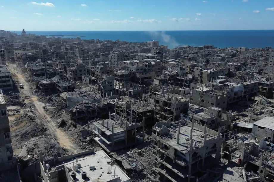 “May Your Problems Always Be So Small”: Palestinian Pain, Pakistani Silence An aerial drone shot captures vast, dense fields of destroyed concrete buildings and leveled blocks in Gaza stretching toward a calm blue sea, creating a somber visual contrast against the backdrop of Palestinian pain and Pakistani silence.