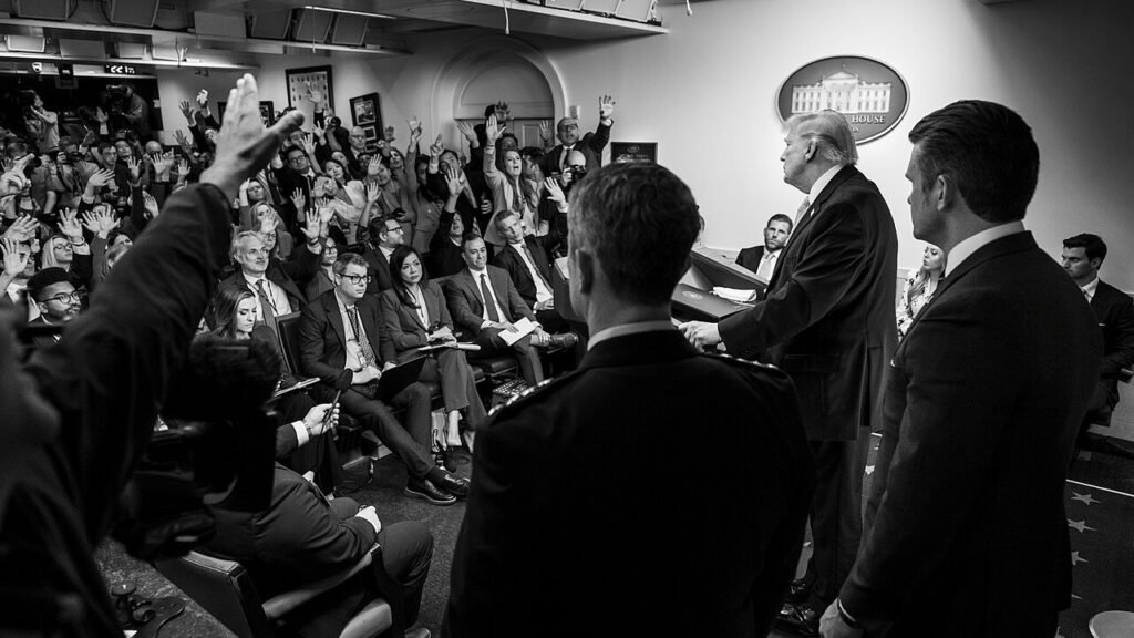 President Donald Trump addressing a packed White House press briefing room with reporters raising hands, as scrutiny mounts over his administration's policy of striking out on Iran.