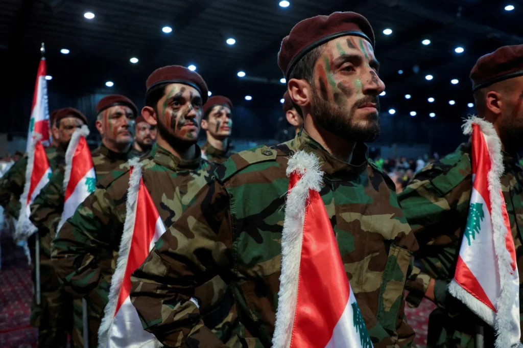 Hezbollah members stand in formation wearing military camouflage uniforms, berets, and face paint while holding Lebanese flags during a parade, illustrating why Hezbollah Remains Iran's Most Important Ally.