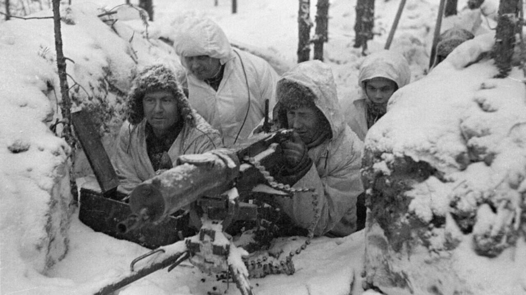 A historical black-and-white photograph of Soviet soldiers in winter gear operating a heavy Maxim machine gun nest in a snowy forest trench, drawing geopolitical parallels to America's Winter War.