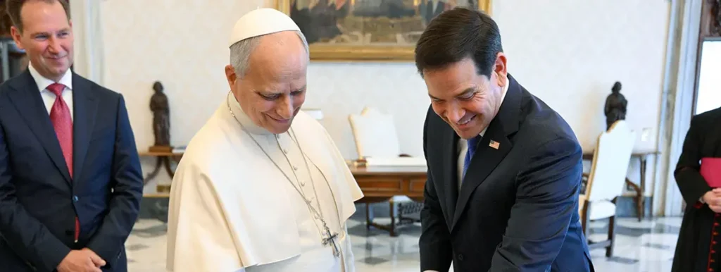 We Don’t Do God’: Reappraising Religious Understanding in Foreign Policy Pope Francis in white vestments stands next to US official Marco Rubio in a dark suit as they both smile and look downward during a formal meeting, highlighting the intersection of global diplomacy and religious understanding.