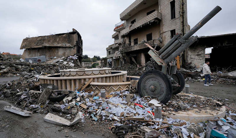 A Lebanon Ceasefire is Just a Poison Pill An artillery gun stands on a street surrounded by heavily damaged buildings, concrete debris, and scattered rubble under a cloudy sky, illustrating the fragile security landscape tied to the discussion of a Lebanon Ceasefire.